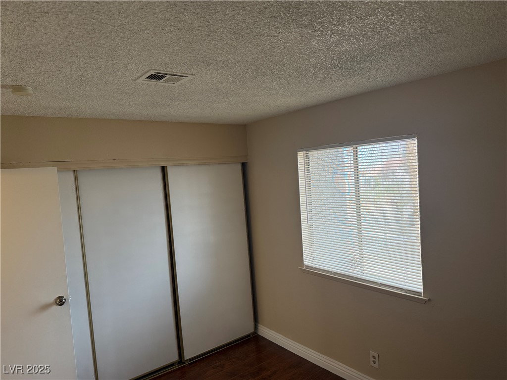 4689 West Sand Creek Avenue, Unit C Las Vegas, NV 89103 - Photo 8 of 14 Unfurnished bedroom featuring dark wood-style flooring, a textured ceiling, and a closet