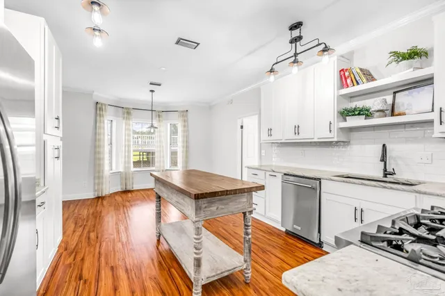 a kitchen with stainless steel appliances granite countertop a refrigerator a stove top oven a sink dishwasher and white cabinets with wooden floor