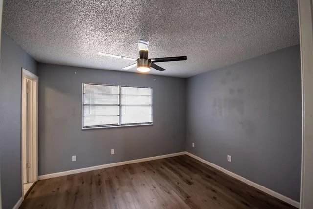 an empty room with wooden floor ceiling fan and windows