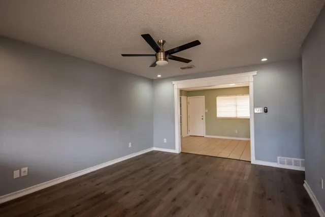 an empty room with wooden floor fan and windows