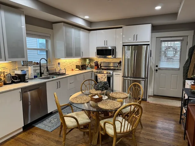 a kitchen with refrigerator a sink dishwasher a dining table and chairs with wooden floor