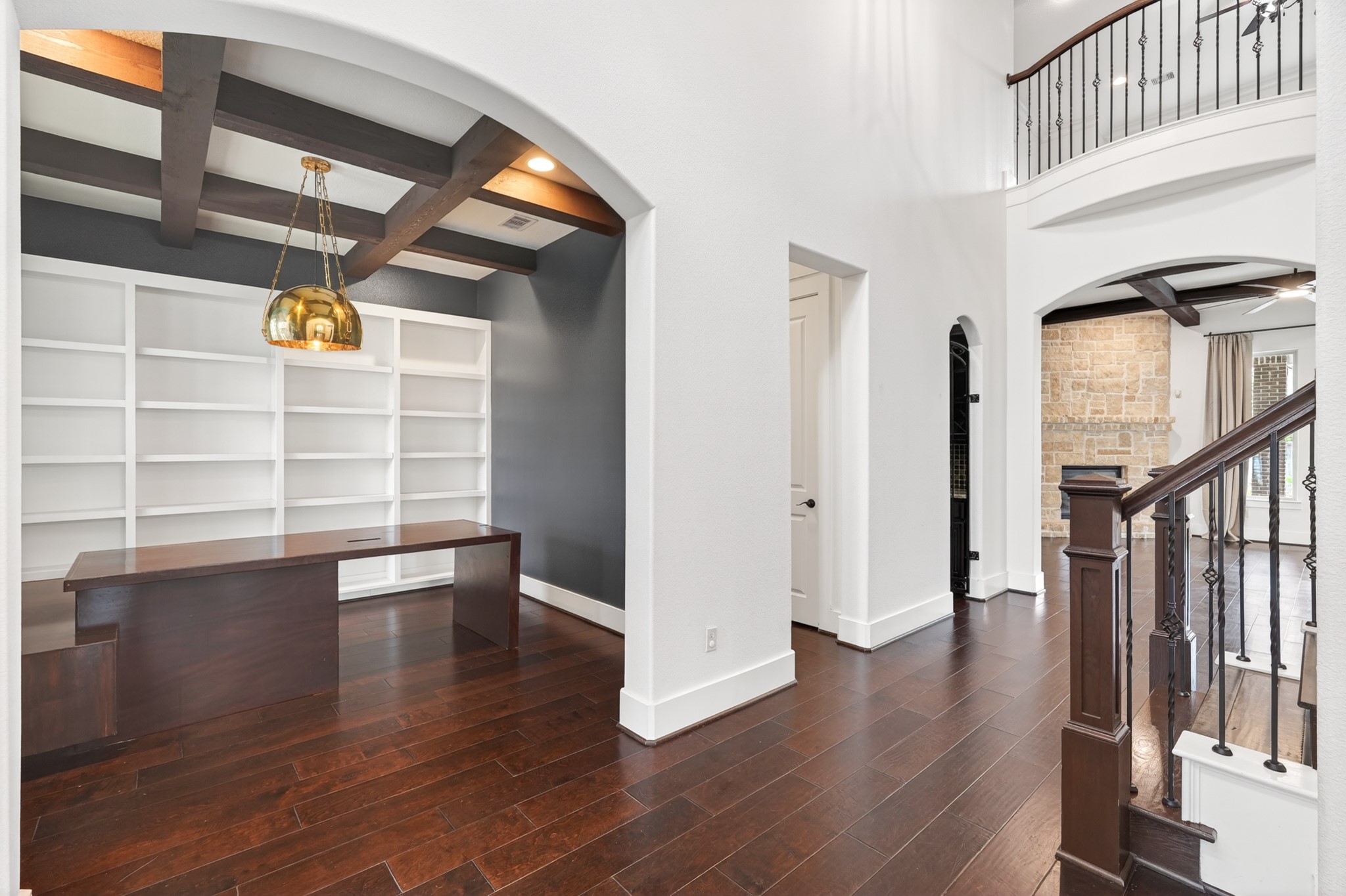 27 Hedgedale Way Spring, TX 77389 - Photo 14 of 43 Original photo shown for reference. Elegant home office featuring rich wood flooring, built-in shelving, and exposed beam ceiling, seamlessly connected to a spacious entryway with wrought iron accents and a stone wall feature. Desk can be included in sale of the home.