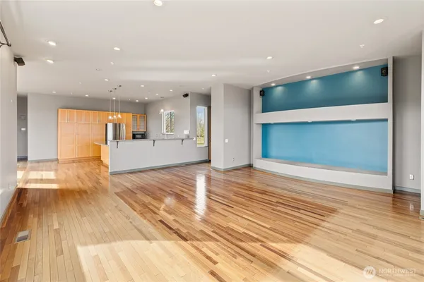 a view of an empty room with wooden floor and a kitchen