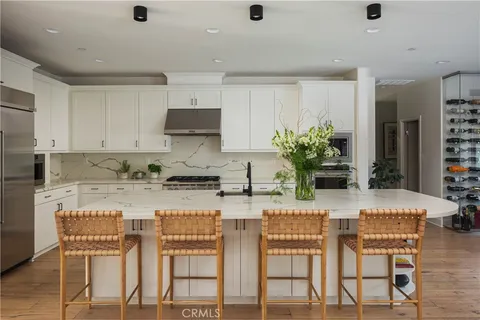 a kitchen with stainless steel appliances kitchen island granite countertop a dining table chairs and white cabinets