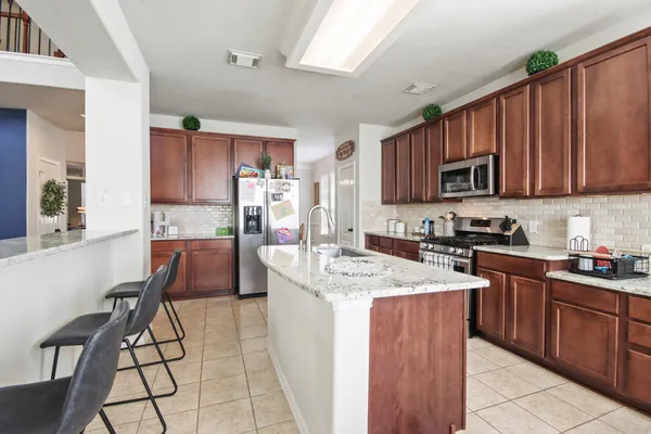 a kitchen with stainless steel appliances granite countertop a stove top oven a sink dishwasher and a refrigerator with wooden cabinets