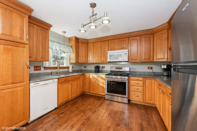 a kitchen with stainless steel appliances granite countertop wooden cabinets a sink a stove a refrigerator and island with wooden floor