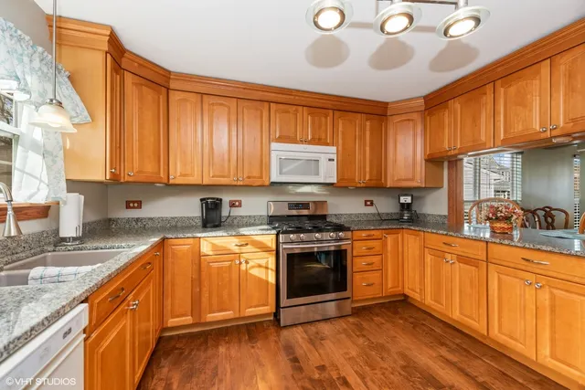 a kitchen with stainless steel appliances granite countertop wooden cabinets a stove a sink and dishwasher with wooden floor