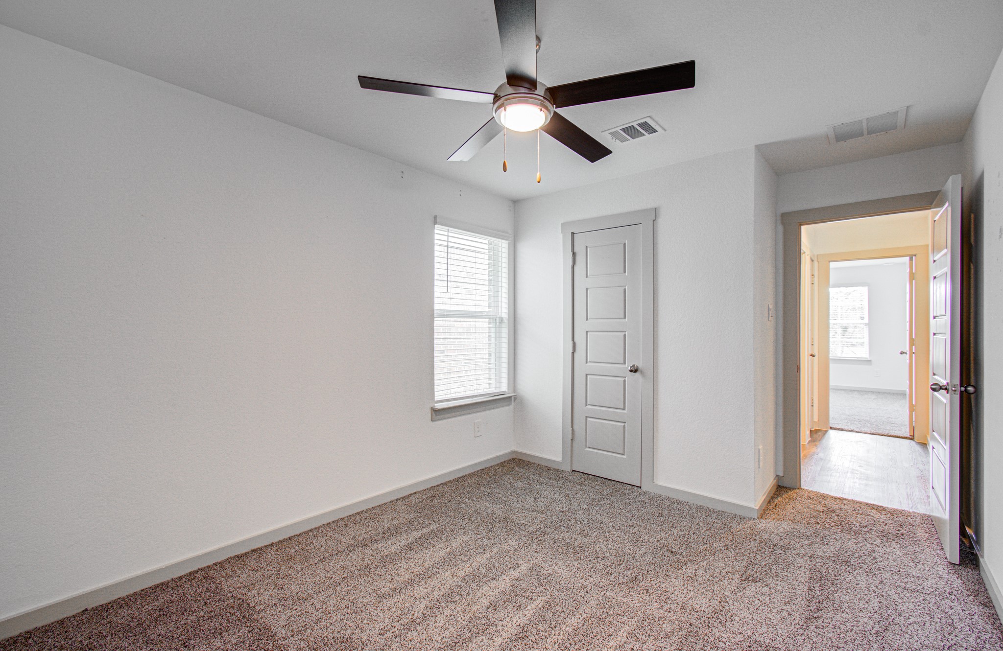7903 Wrangler Shack Lane Rosharon, TX 77583 - Photo 9 of 29 This bright, carpeted bedroom features neutral walls, a ceiling fan, and ample natural light, with a modern door leading to an adjacent room, hinting at a spacious and inviting layout.