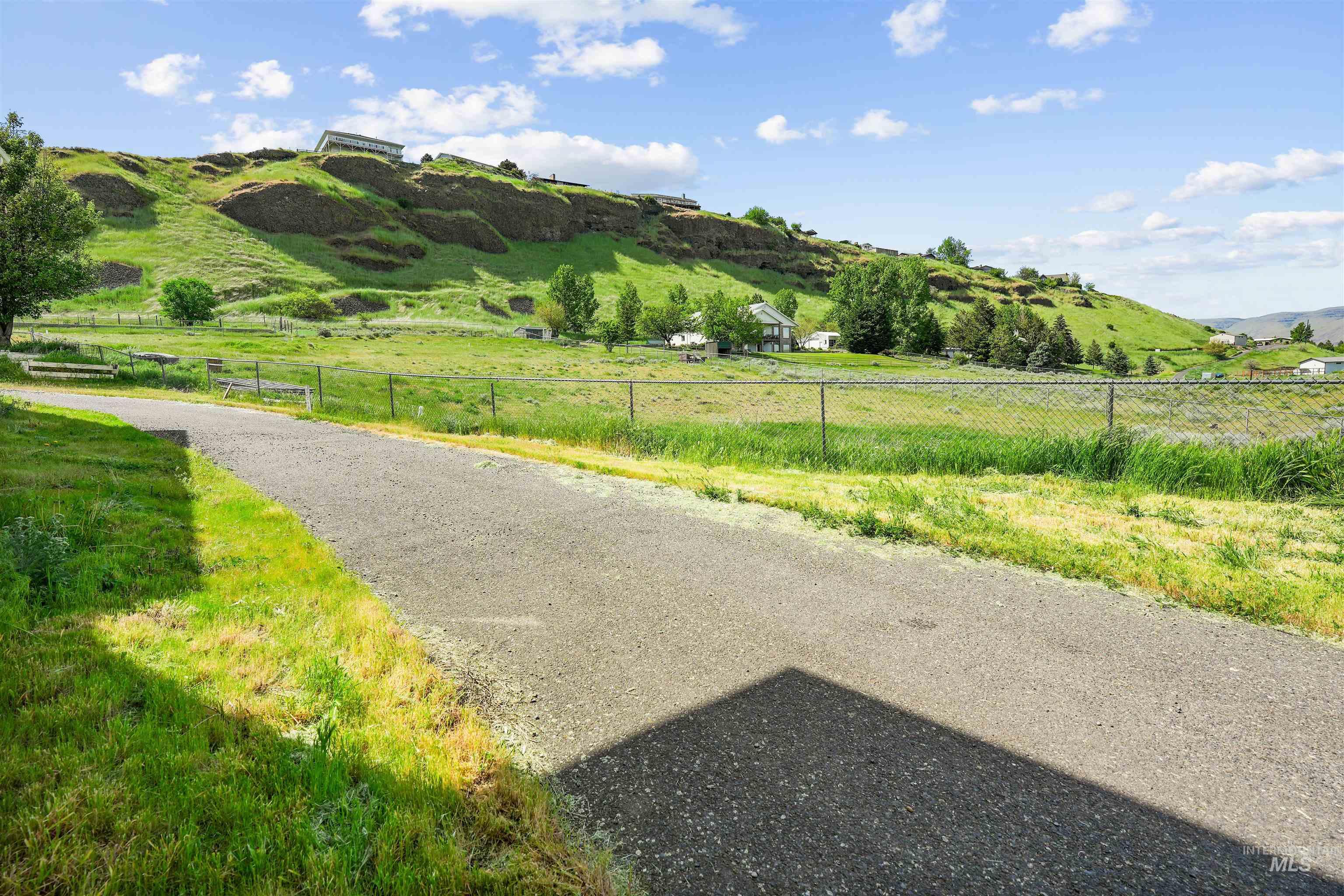 2750 South Perry Lane Clarkston, WA 99403 - Photo 11 of 47 Paved pathway bordered by green grass, chain-link fencing, and a distant hillside with scattered structures
