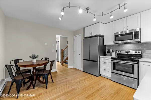 a kitchen with stainless steel appliances a dining table chairs refrigerator and microwave
