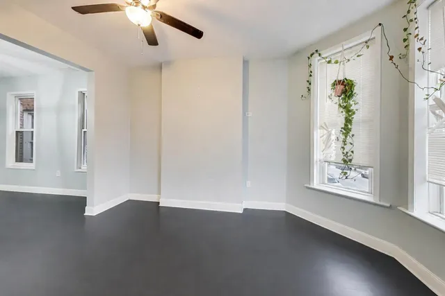 an empty room with wooden floor chandelier fan and windows