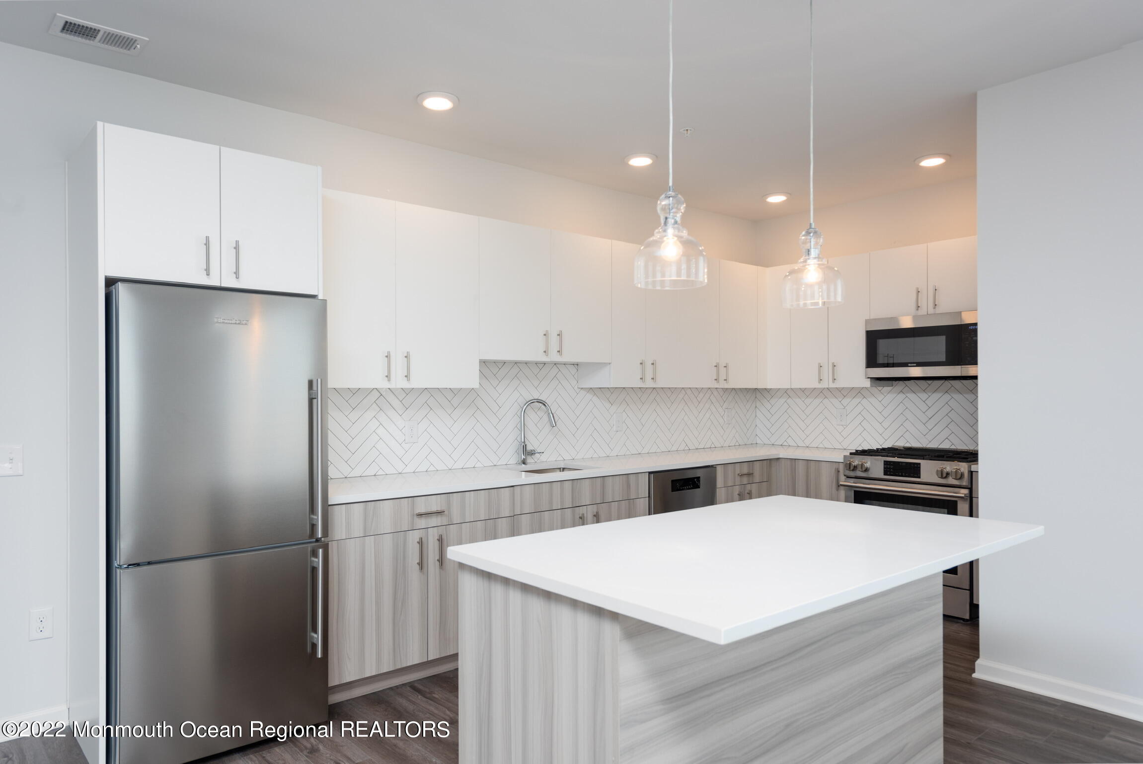a kitchen that has a refrigerator a stove a sink and white cabinets with wooden floor