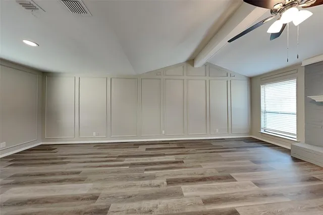 a view of an empty room with wooden floor and fan