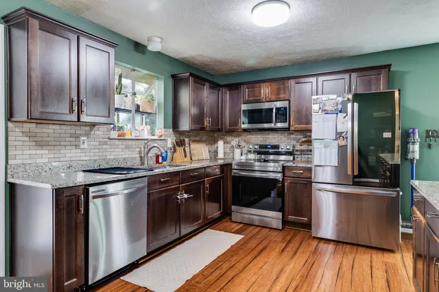 a kitchen with stainless steel appliances granite countertop a stove top oven a sink dishwasher a dining table and chairs with wooden floor