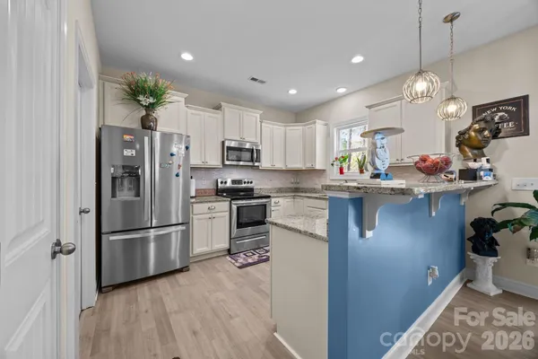 a kitchen with stainless steel appliances granite countertop a refrigerator a sink dishwasher a stove and white cabinets with wooden floor