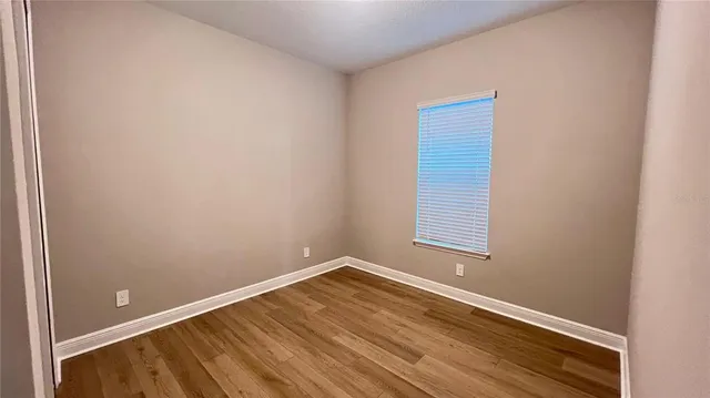 a view of an empty room with wooden floor and a window
