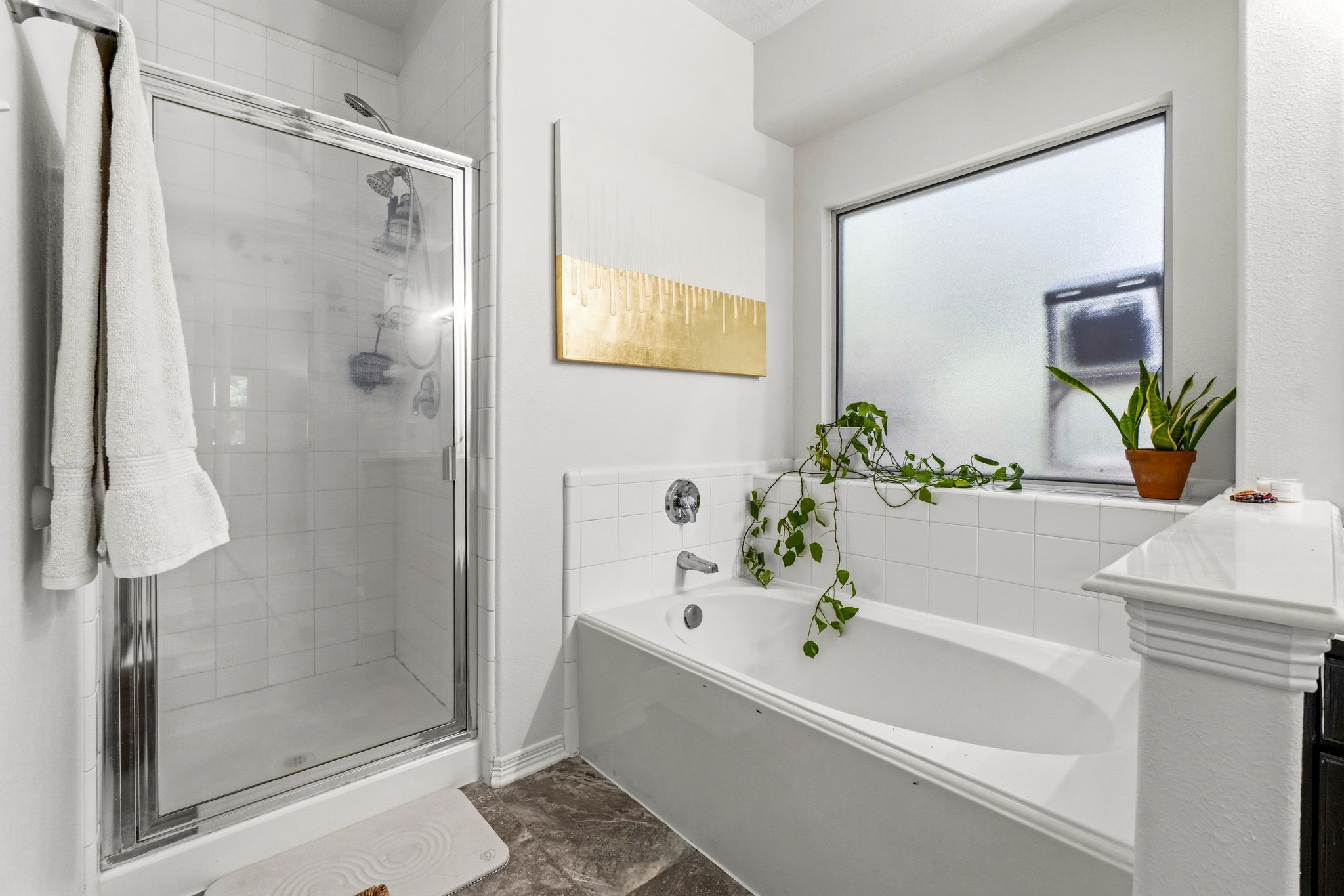 34019 Conroe Huffsmith Road Magnolia, TX 77354 - Photo 13 of 19 Modern bathroom featuring a glass-enclosed shower and a separate bathtub. It has a frosted window for privacy, elegant tile work, and decorative plants that add a touch of nature.