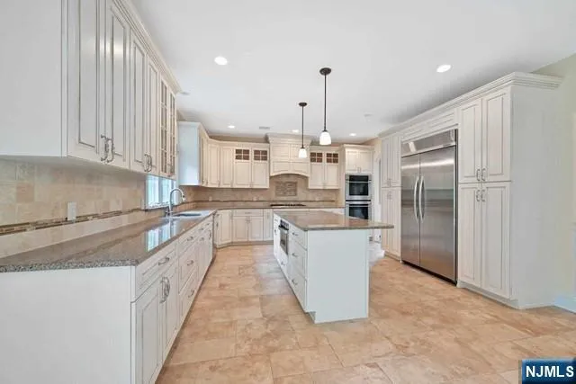 a large kitchen with stainless steel appliances kitchen island granite countertop a refrigerator a sink and a stove
