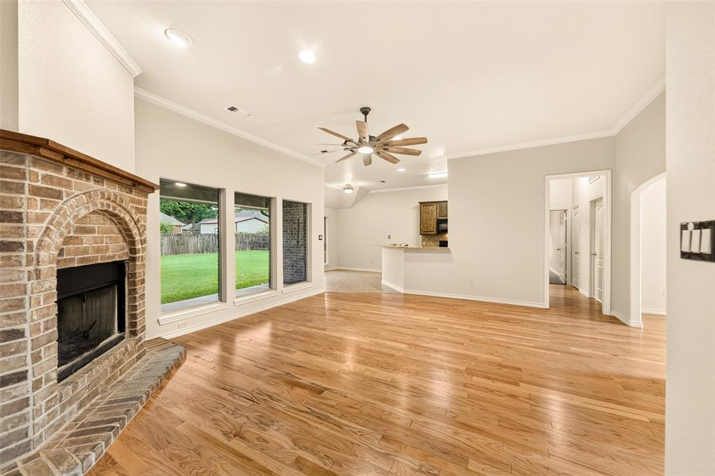 2105 Ridgewood Drive Bridgeport, TX 76426 - Photo 9 of 27 Living area featuring wood-finish flooring, a brick fireplace with a hearth, and a vaulted ceiling with crown molding
