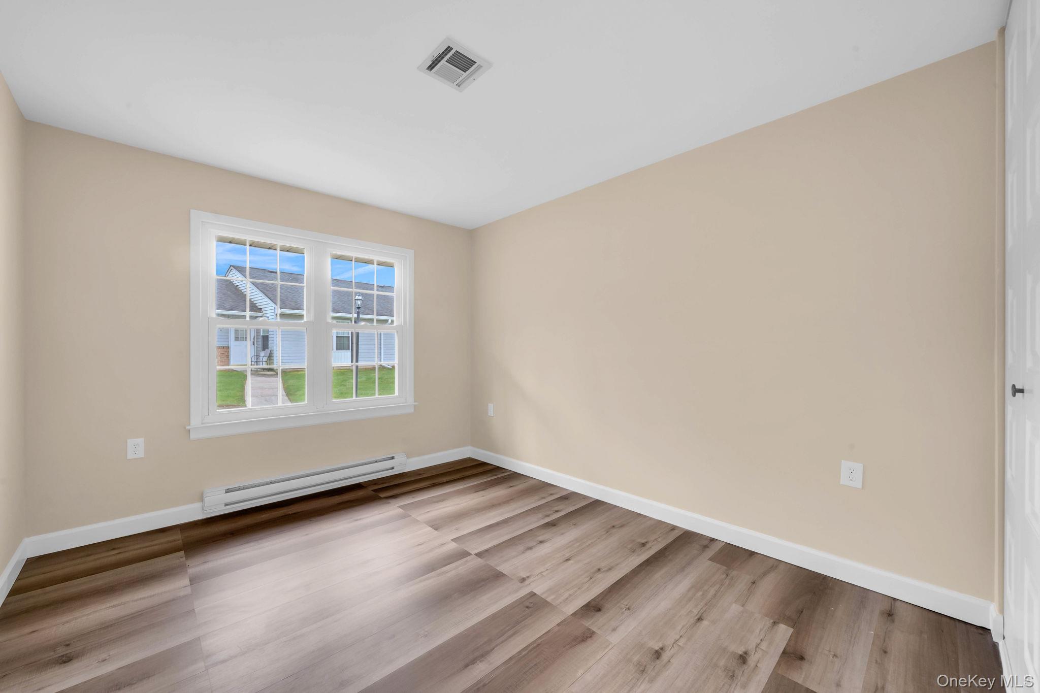 380 Woodbridge Drive, Unit D Ridge, NY 11961 - Photo 13 of 25 an empty room with wooden floor and windows