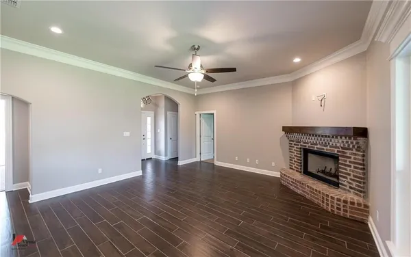 an empty room with wooden floor a ceiling fan a fireplace and windows