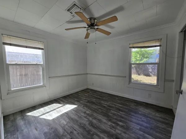 an empty room with wooden floor fan and windows