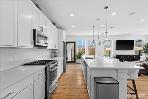 a kitchen with stainless steel appliances a stove a sink a microwave a refrigerator and white cabinets