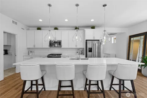 a kitchen with stainless steel appliances kitchen island granite countertop a dining table chairs and a refrigerator