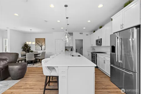 a kitchen with stainless steel appliances kitchen island granite countertop a refrigerator a stove a sink a dining table and chairs with wooden floor