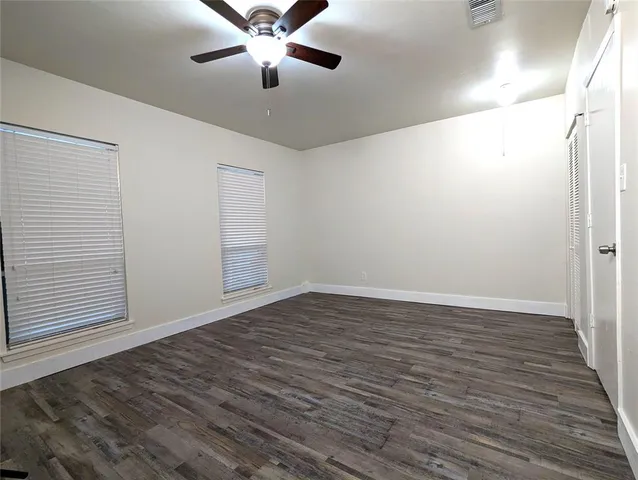 an empty room with wooden floor fan and windows