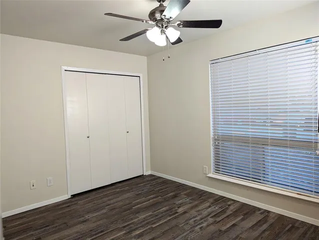 a view of an empty room with wooden floor and a ceiling fan