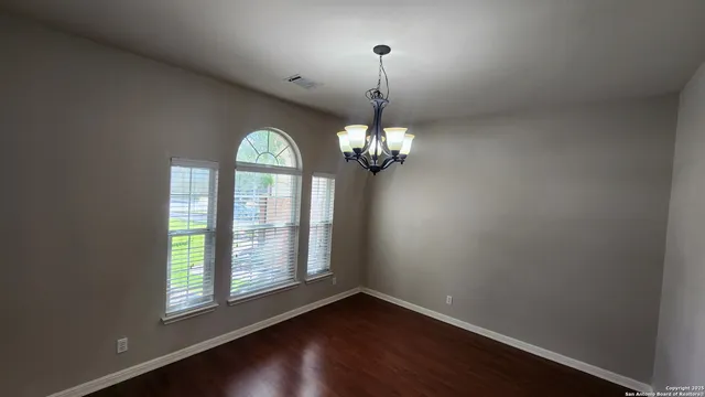 an empty room with wooden floor chandelier and windows