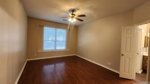 an empty room with wooden floor chandelier fan and windows