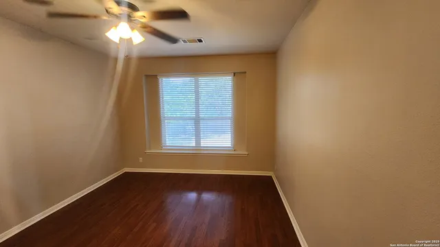 an empty room with wooden floor fan and windows