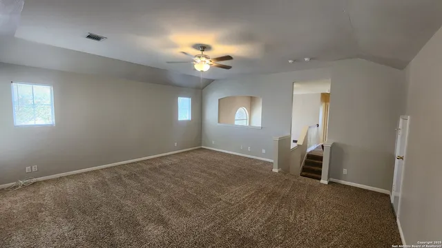 an empty room with a chandelier fan and windows