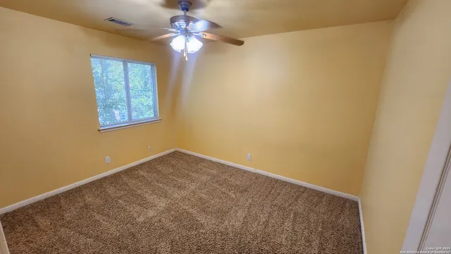 an empty room with a chandelier fan and windows