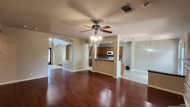 a view of an empty room and kitchen with a ceiling fan