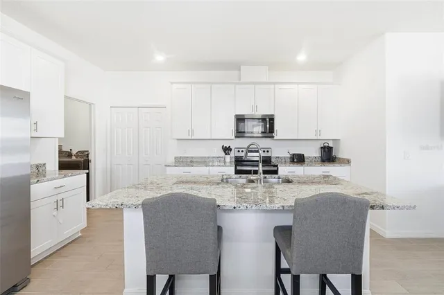 a kitchen with stainless steel appliances granite countertop a stove a sink a microwave a refrigerator and white cabinets