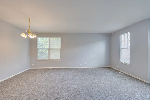 an empty room with chandelier fan and windows