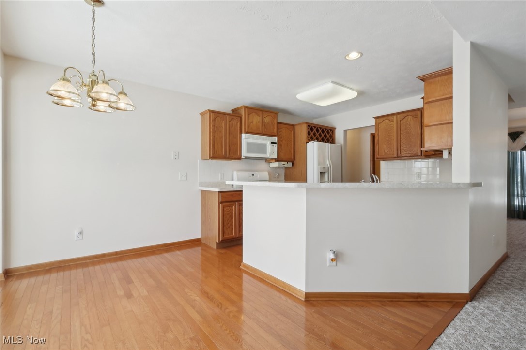 15139 Timber Ridge Drive Middlefield, OH 44062 - Photo 9 of 44 Kitchen With Wood Flooring, White Appliances, Breakfast Bar, and Hanging Light Fixture