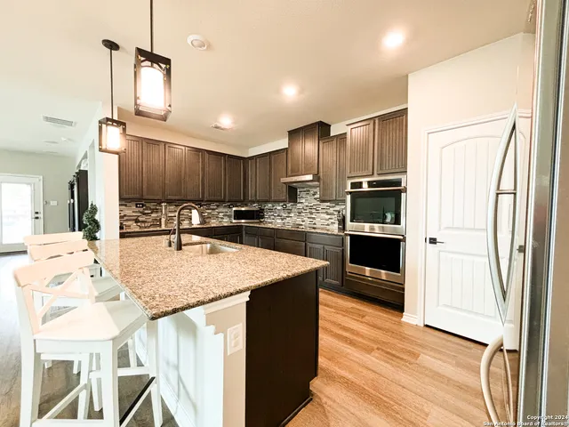 a kitchen with stainless steel appliances kitchen island granite countertop a refrigerator a stove and a sink with wooden floor