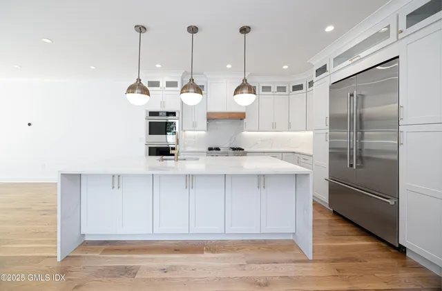 a view of a kitchen with stainless steel appliances granite countertop a refrigerator a sink and a wooden floor