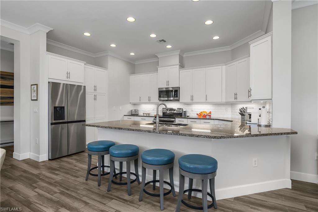 6907 Cay Court Naples, FL 34113 - Photo 19 of 50 Kitchen with a peninsula, stainless steel appliances, dark stone counters, white cabinetry, and recessed lighting.