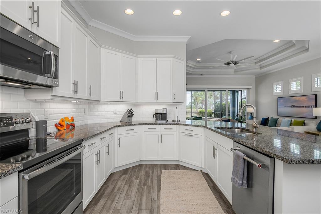 6907 Cay Court Naples, FL 34113 - Photo 25 of 50 Kitchen featuring stainless steel appliances, crown molding, white cabinetry, dark stone counters, and a peninsula