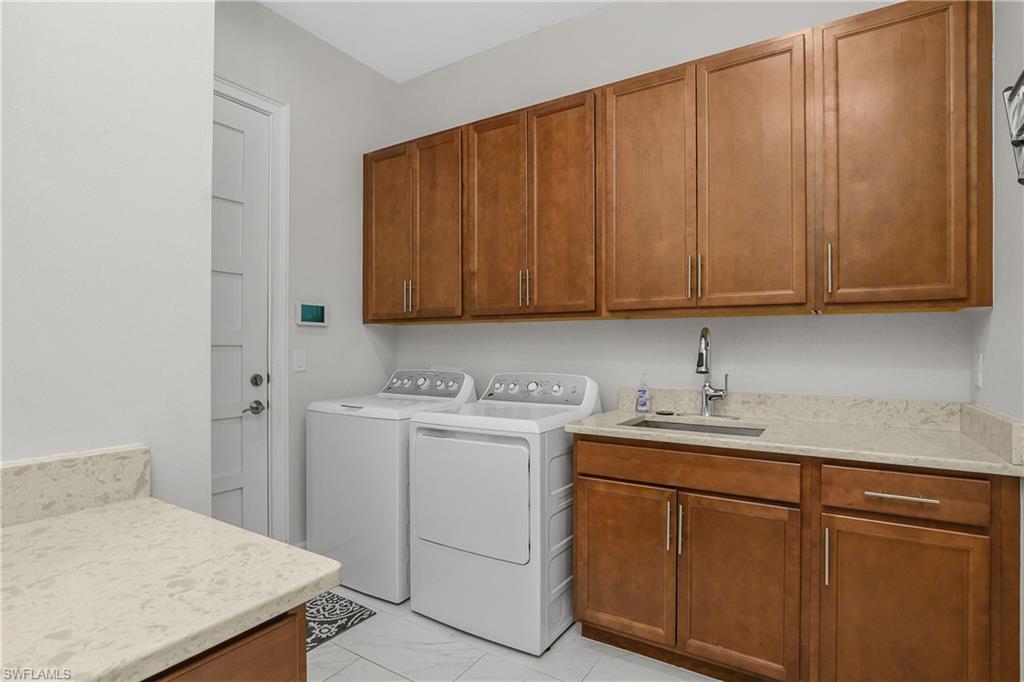 6907 Cay Court Naples, FL 34113 - Photo 36 of 50 Large Laundry area with washer and dryer, sink, cabinet space, and light marble finish flooring.