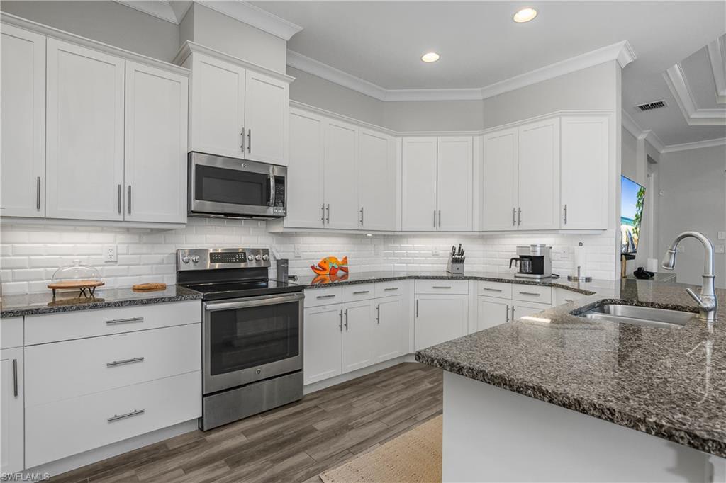6907 Cay Court Naples, FL 34113 - Photo 5 of 50 Kitchen with stainless steel appliances, white cabinetry, dark stone counters, crown molding, and backsplash