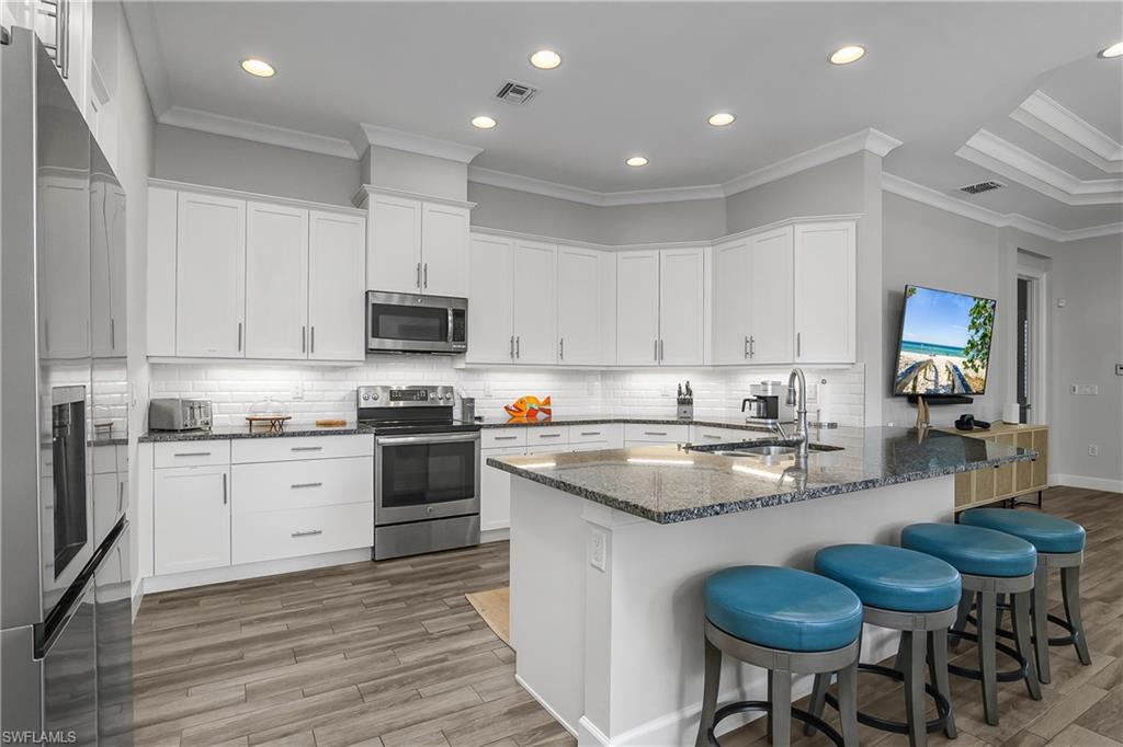 6907 Cay Court Naples, FL 34113 - Photo 6 of 50 Kitchen featuring a breakfast bar, a peninsula, ornamental molding, stainless steel appliances, and dark stone countertops
