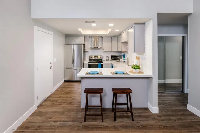 a kitchen with stainless steel appliances a stove a sink a refrigerator white cabinets and wooden floor