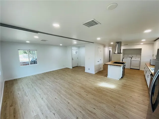 a view of an empty room with wooden floor and a kitchen