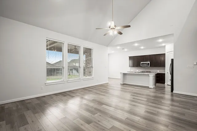 a view of an empty room with kitchen and window